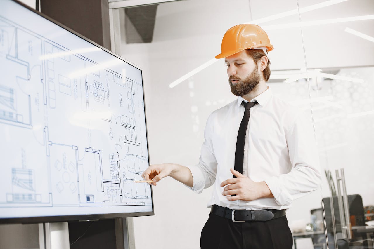 hero-img Architect in hard hat reviewing blueprints on a screen, discussing plans in modern office.